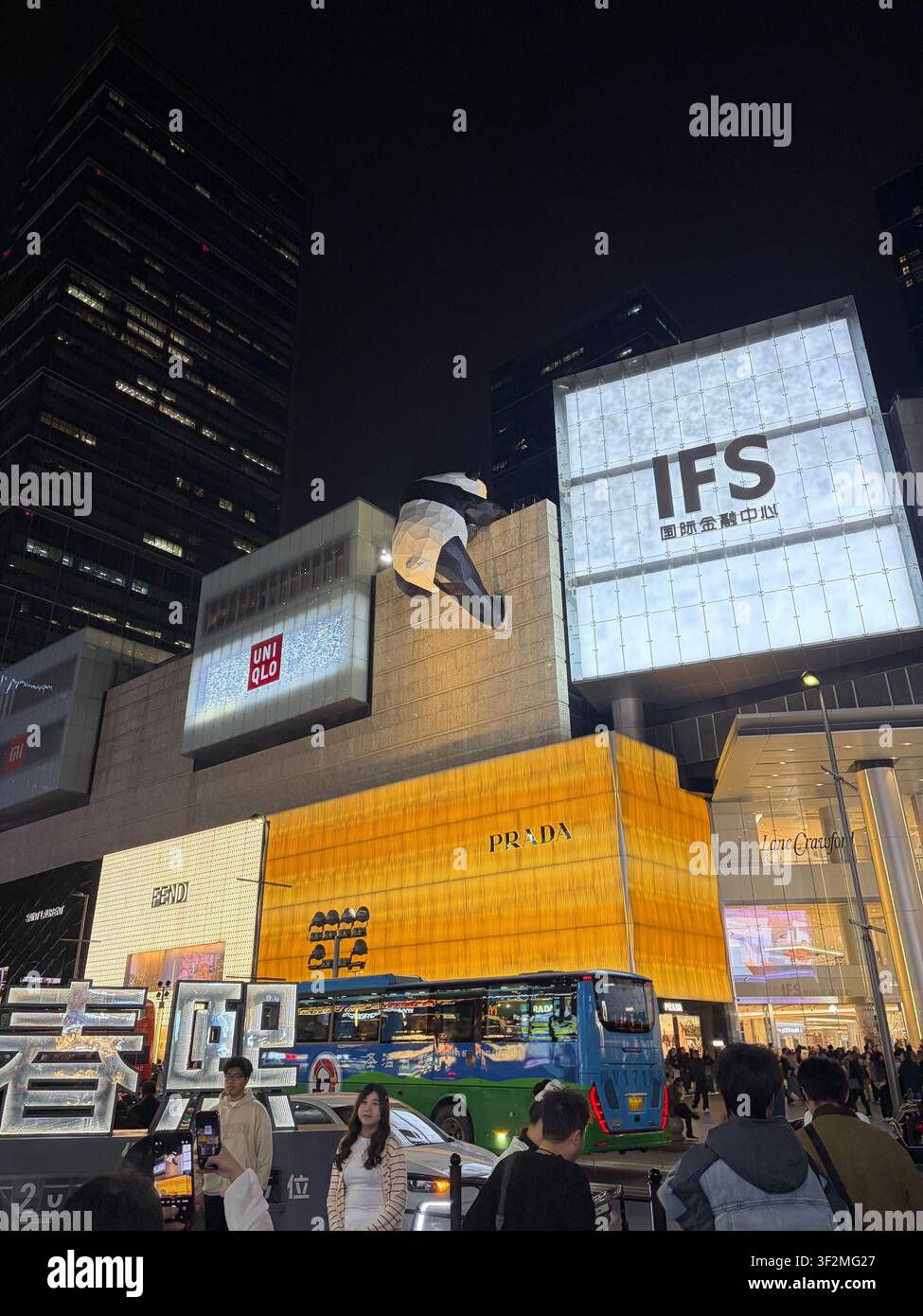 13. November 2025, Chengdu, Sichuan, China – Iconische Riesengorilla-Skulptur klettert an der Fassade des IFS-Luxus-Einkaufszentrums bei Nacht mit Prada-, Uniqlo- und Fendi-Schaufenstern. - Smartphone-aufgenommenes Stockfoto