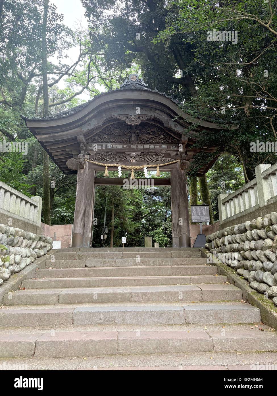 3. September 2025, Kanazawa, Japan – Aufwendig geschnitztes Holztor (Karamon) eines Shintoschreins, umgeben von uralten Bäumen, Steinlaternen und moosbewachsenen Bauten. - Smartphone-aufgenommenes Stockfoto