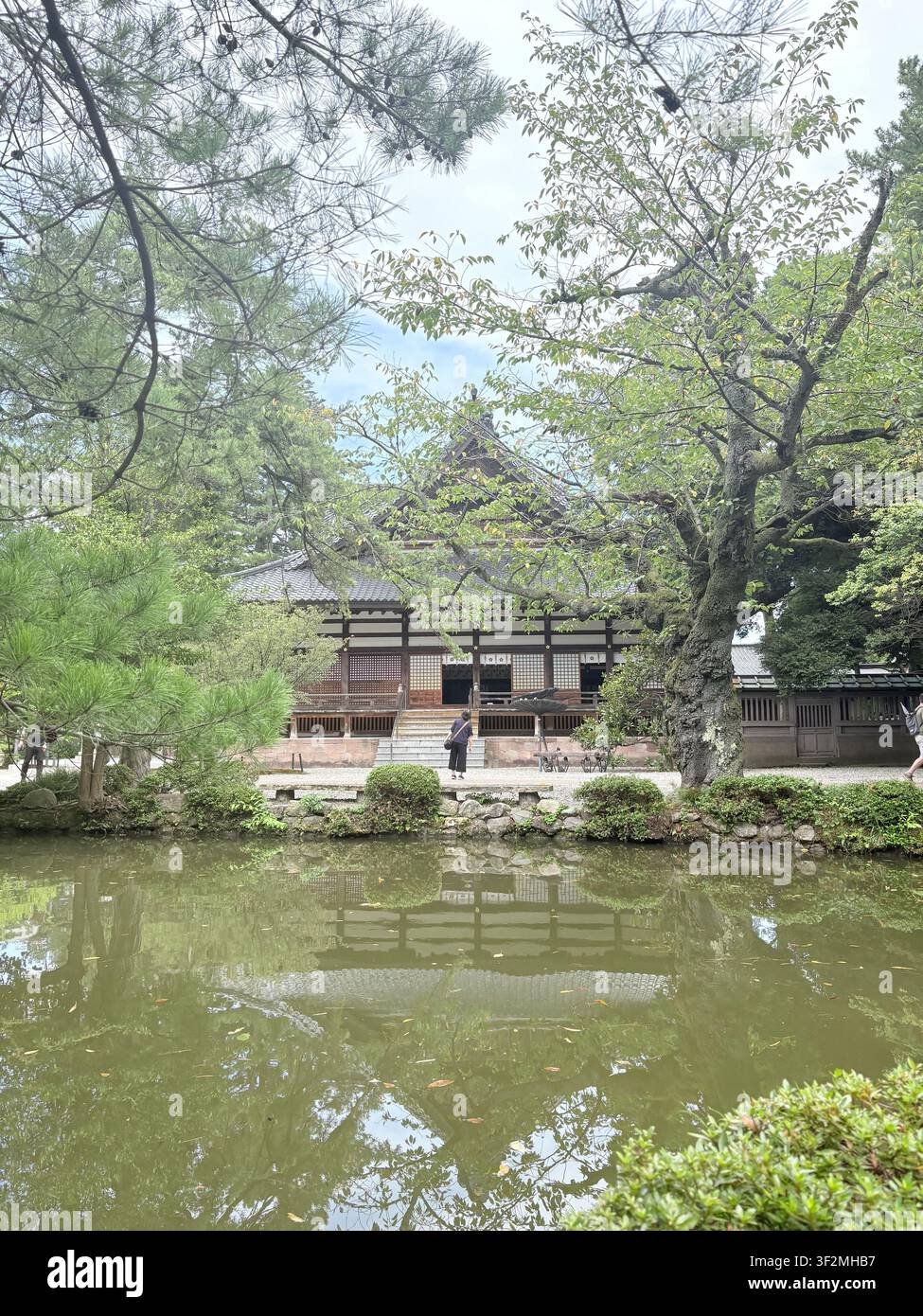 3. September 2025, Kanazawa, Japan – Traditioneller hölzerner Pavillon, umgeben von üppiger Vegetation, spiegelt sich im ruhigen Teichwasser eines historischen japanischen Gartens wider. - Smartphone-aufgenommenes Stockfoto