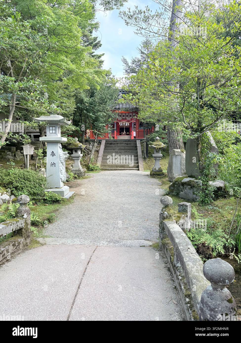 3. September 2025, Kanazawa, Japan – Traditionelle Steinlaternen und rote Shinto-Schreinerstruktur, umgeben von üppiger grüner Vegetation in Kanazawa. - Smartphone-aufgenommenes Stockfoto