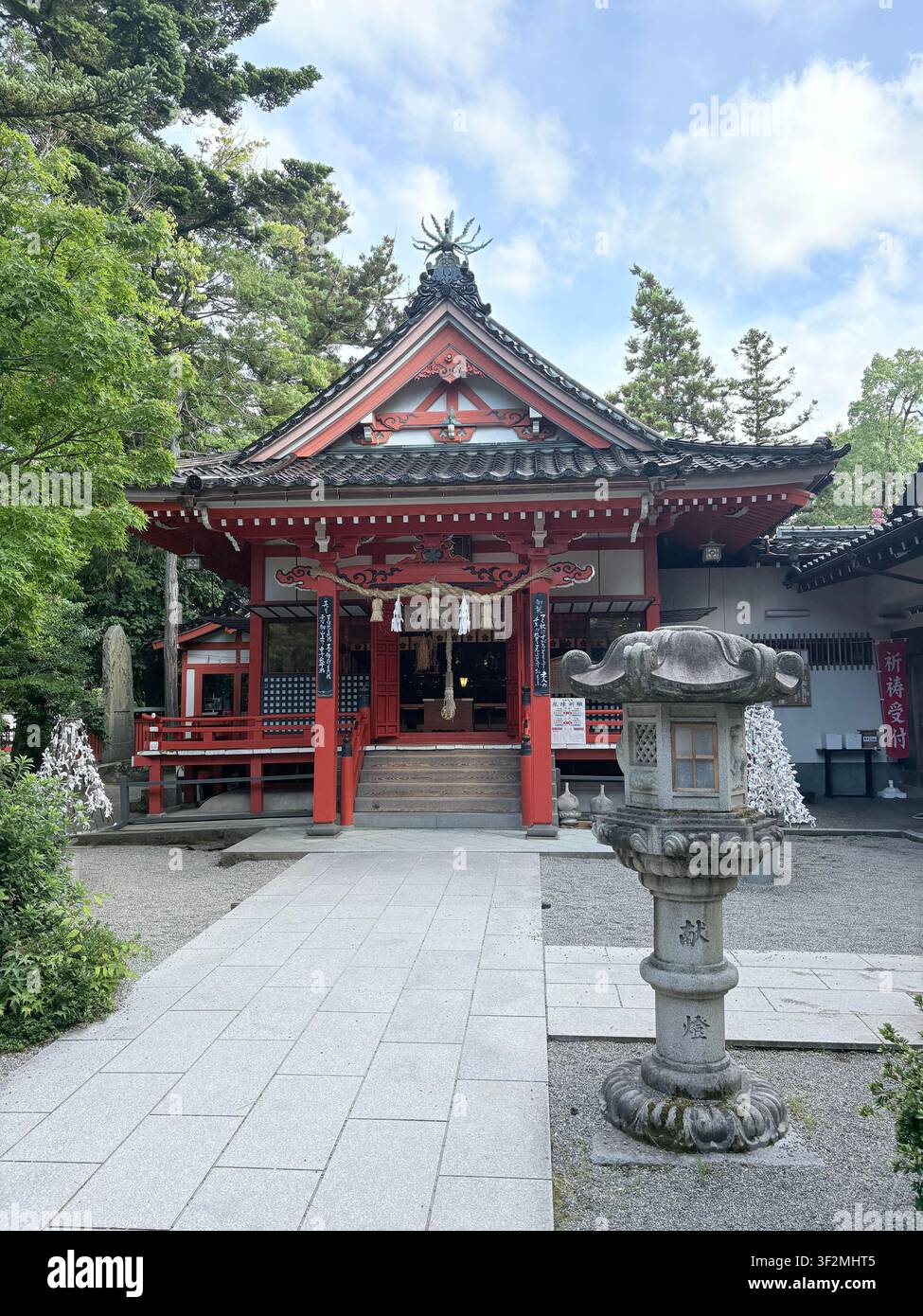 3. September 2025, Kanazawa, Japan – Traditioneller roter Shintoschrein mit kunstvoll geschwungenem Dach, Shimenawa-Seil, Steinlaternen und japanischen Kalligrafie-Bannern in Kanazawa. - Smartphone-aufgenommenes Stockfoto