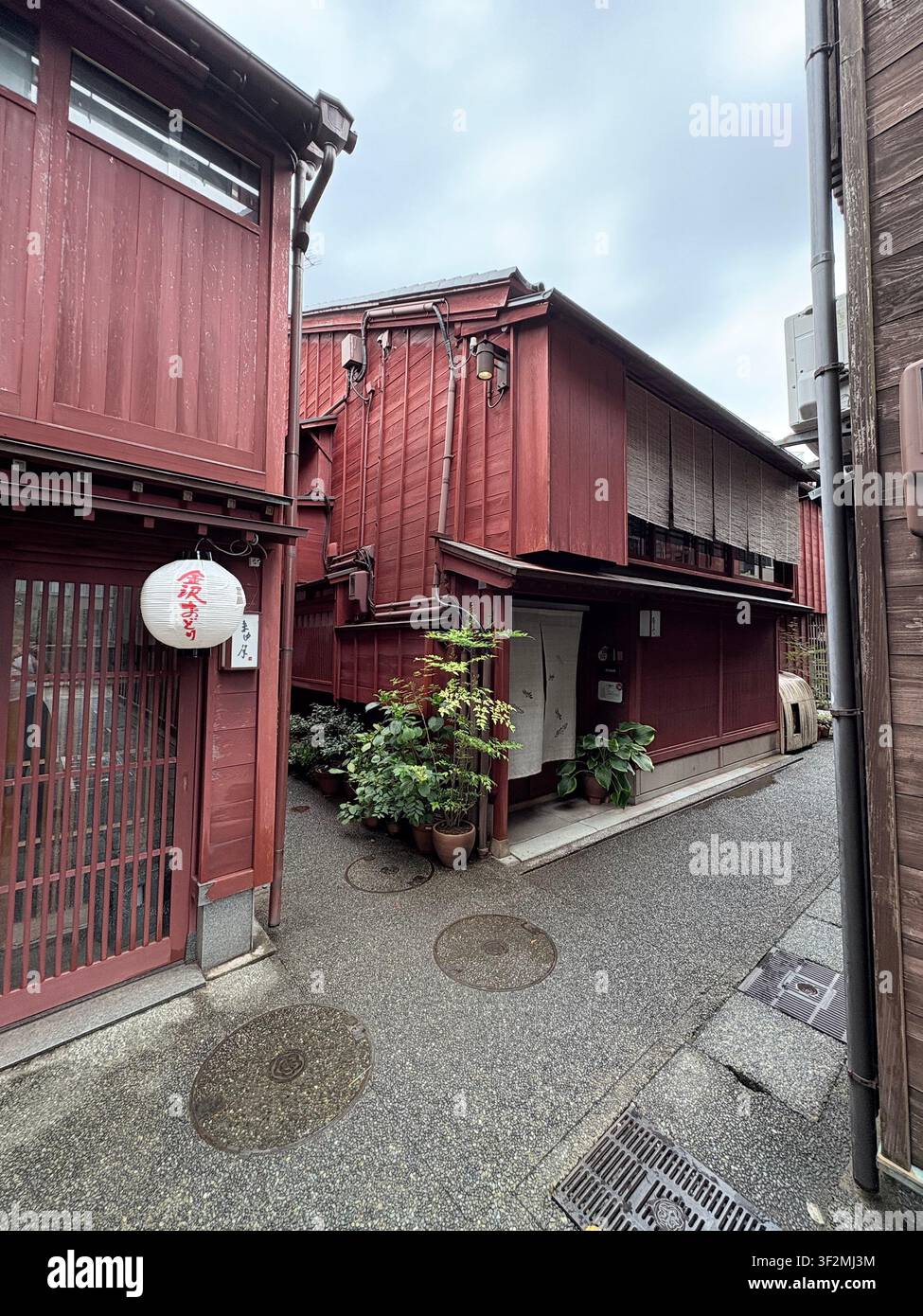 4. September 2025, Kanazawa, Japan – Rot gestrichenes Holz-Machiya-Reihenhaus mit beleuchteter Chocho-Chiranlampe und Topfpflanzen im historischen Viertel von Kanazawa. - Smartphone-aufgenommenes Stockfoto