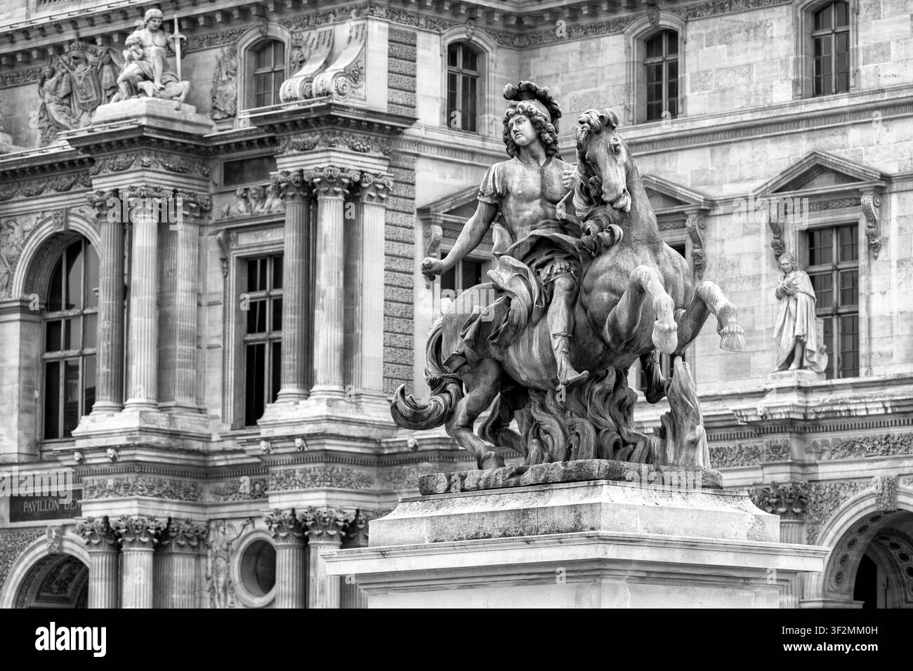 Eine majestätische Reiterstatue von König Ludwig XIV. Ist vor dem reich verzierten historischen Gebäude des Louvre zu sehen. Die detaillierte Bildhauerei Stockfoto