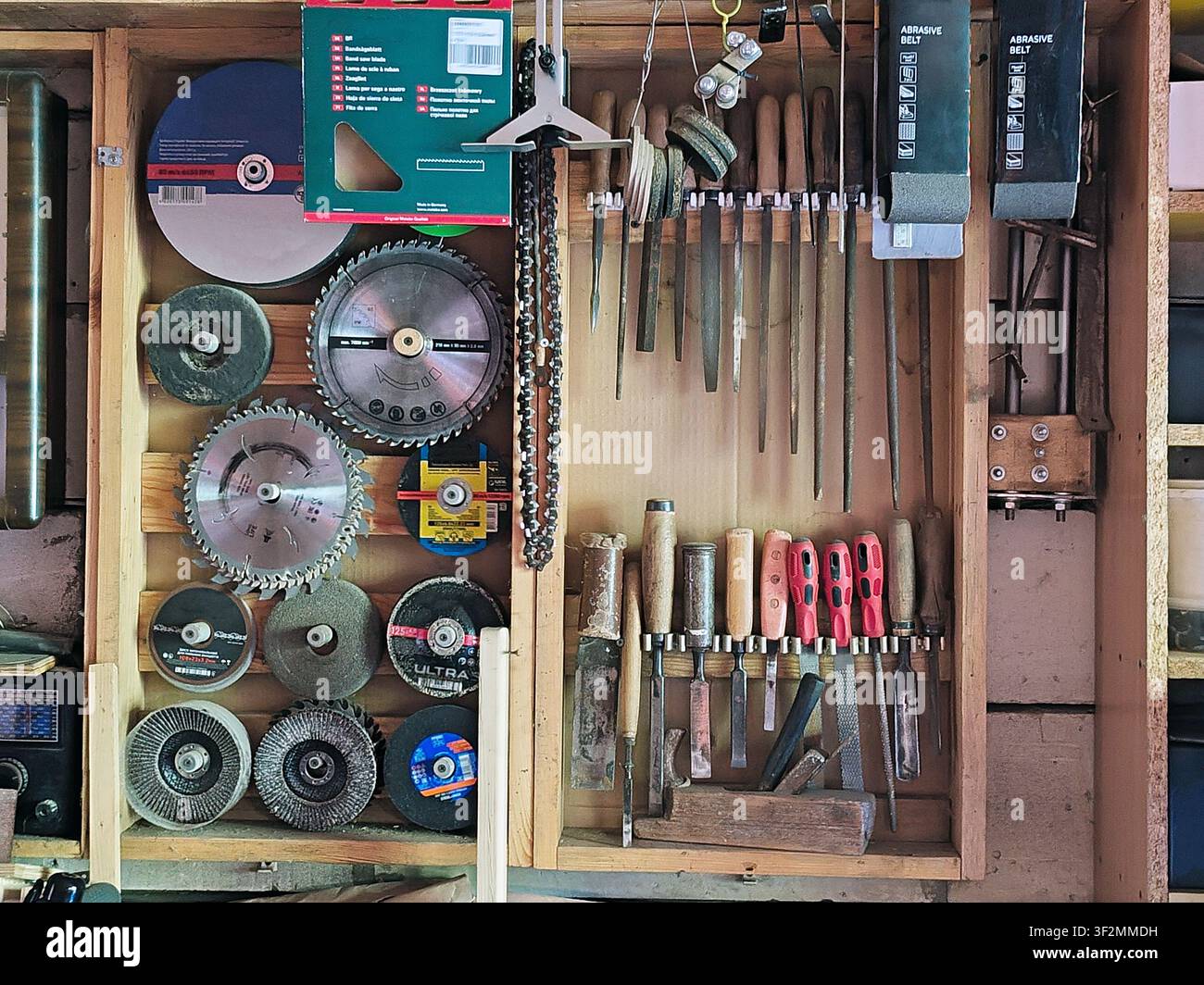 Organisierte Holz- und Metallarbeitswerkzeuge an einer Werkstattwand. Kreissägeblätter, Feilen, Meißel, Schleifscheiben und Handwerkzeuge ordentlich angeordnet in Stockfoto