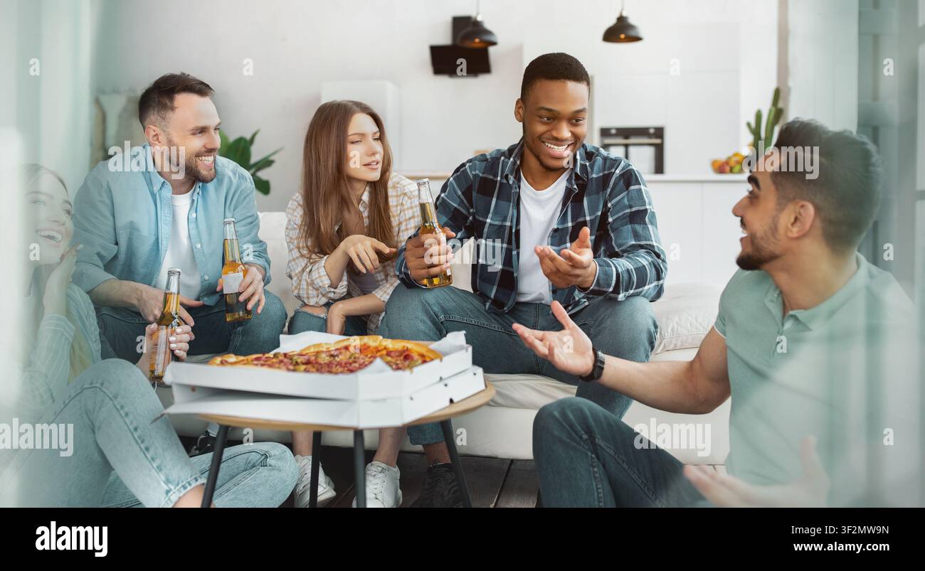 Gruppe von Freunden genießt Pizza und Getränke zu Hause, fröhliche Lächeln, lockere Zusammenkunft Stockfoto