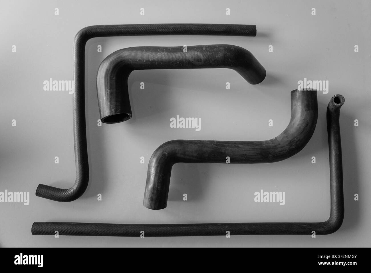 Schwarz-Weiß-Flachlage verschiedener geformter Gummi-Autoschläuche in verschiedenen Formen und Größen, angeordnet auf einem schlichten grauen Hintergrund, zeigt Kühlmittel Stockfoto