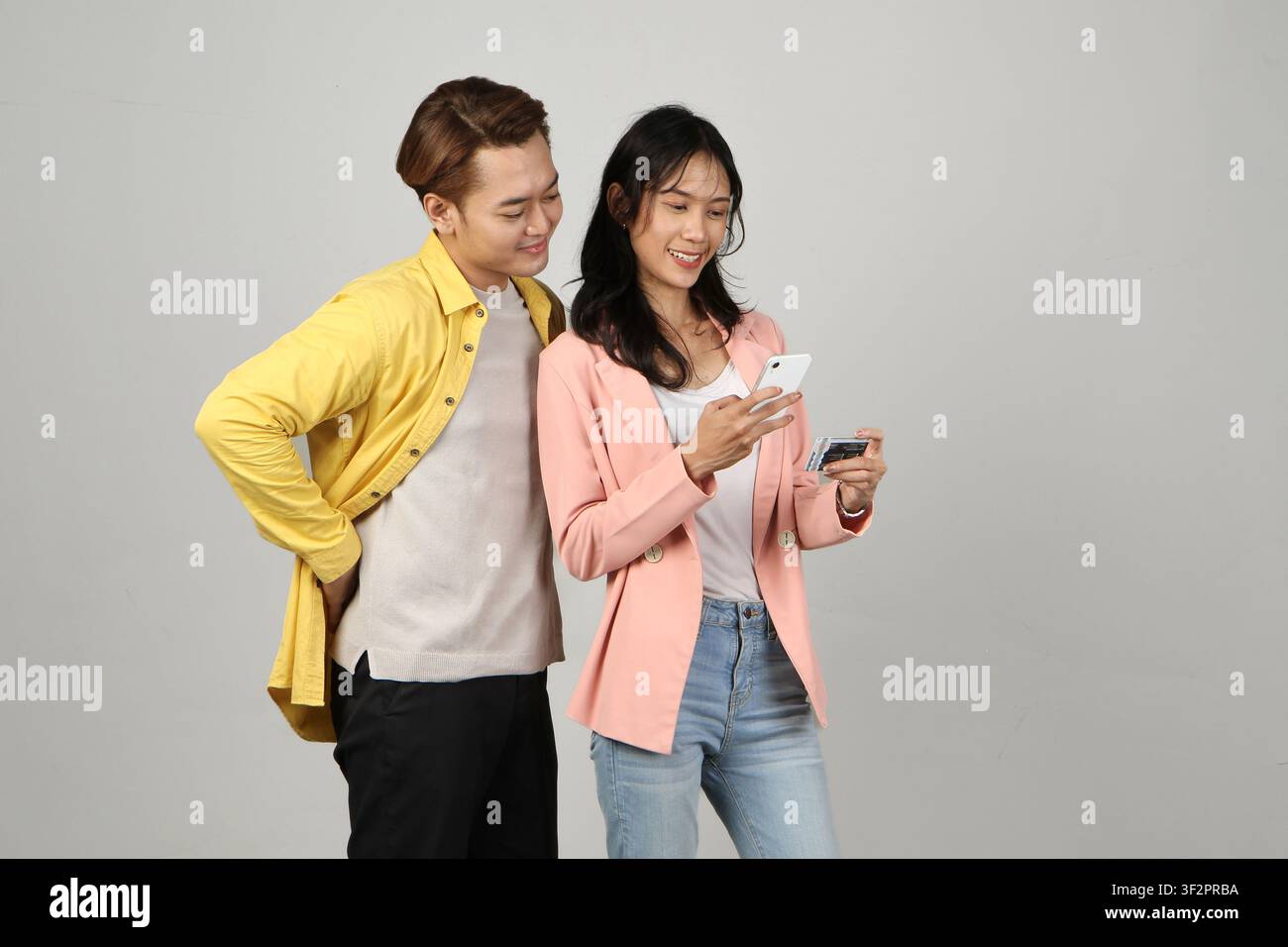 Porträt eines glücklichen asiatischen indonesischen Paares, das ein Smartphone und eine Kreditkarte auf einem isolierten Hintergrund hält. Stockfoto