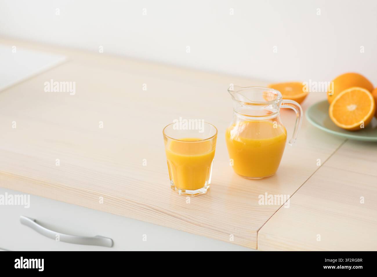 Frisch gepresster Orangensaft aus Glas und Krug, Obst auf Teller auf weißen Möbeln in moderner minimalistischer Küche Stockfoto
