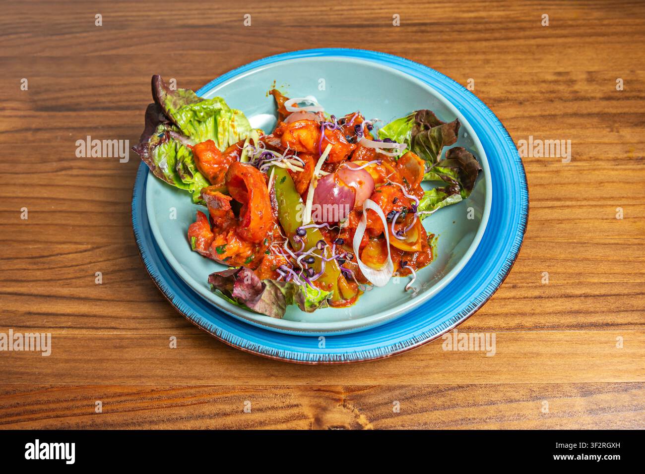 Scharfes Hühner-Karahi mit Paprika und Sprossen auf einem türkisfarbenen Teller serviert Stockfoto