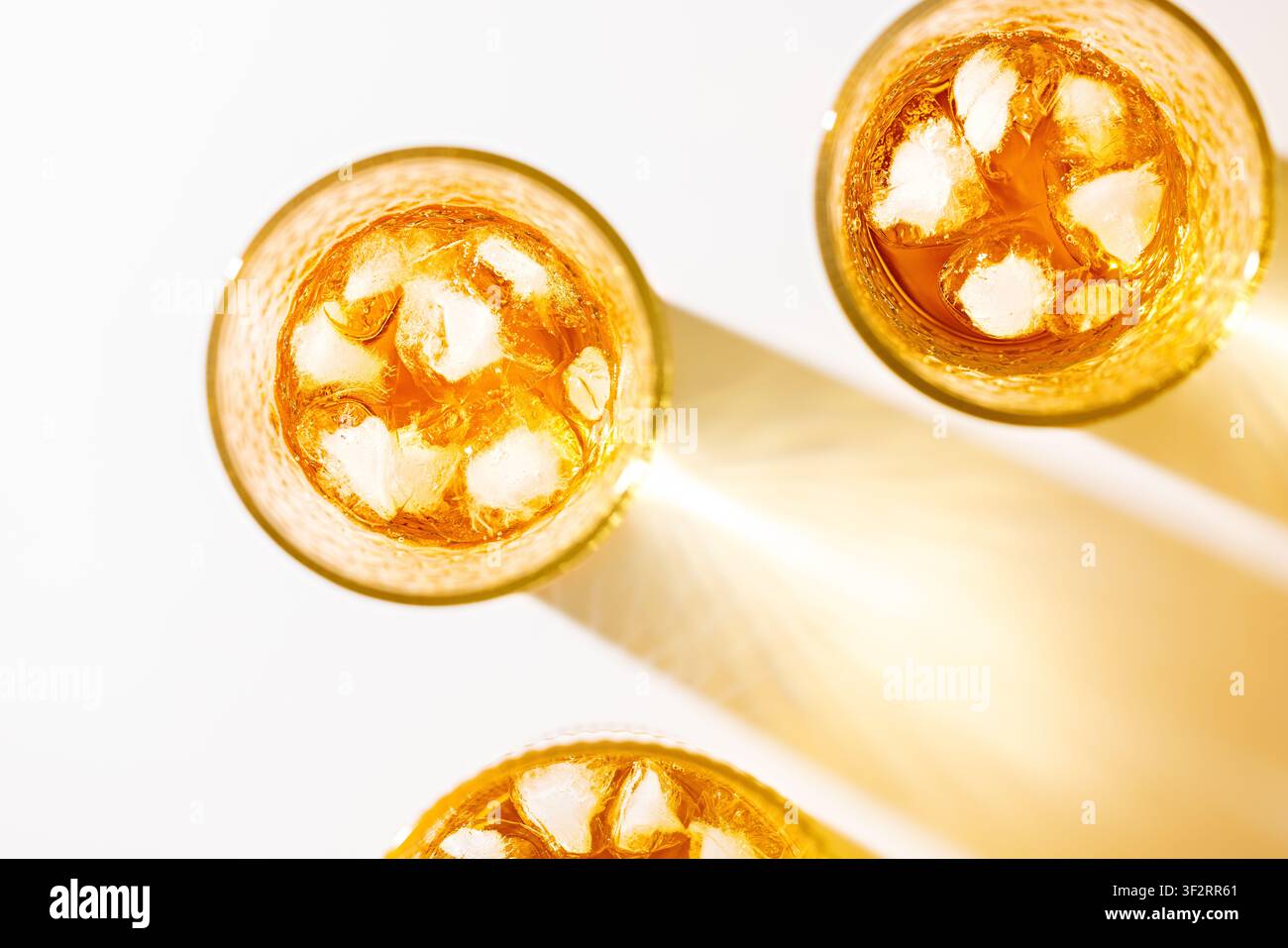 Drei Gläser mit eisgekühltem Apfelsaft mit langen goldenen Schatten auf weißem Sommergetränkehintergrund Stockfoto