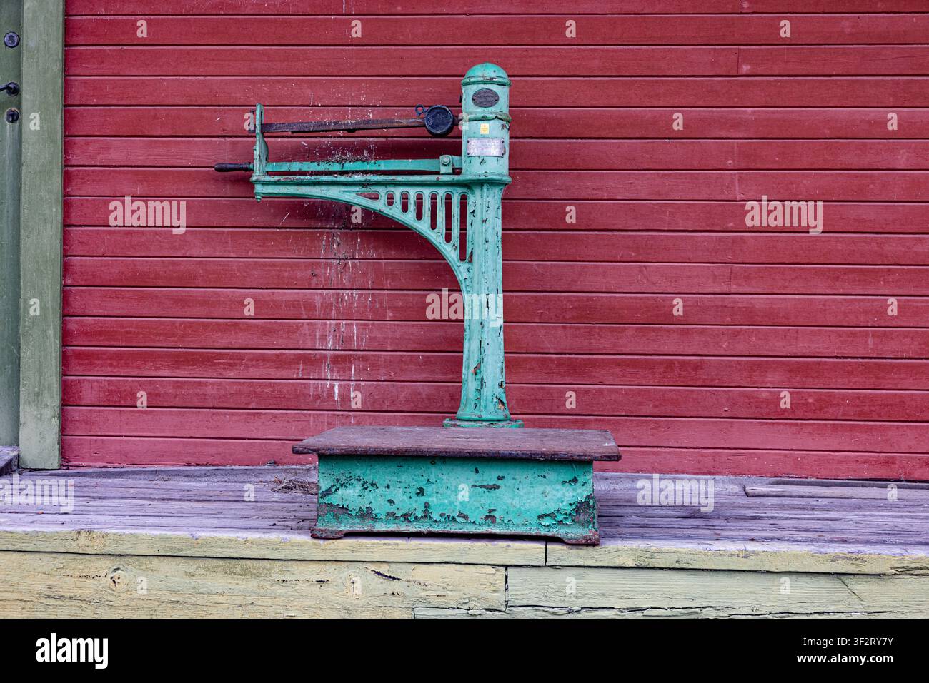 Mel-Stasjon, Rjukanbanen, Norwegen. Eine antike Waage steht vor einer roten Holzwand. Patinierte grüne Farbe zeigt Anzeichen von Witterungseinflüssen. Ihr stabiler Metallrahmen Stockfoto