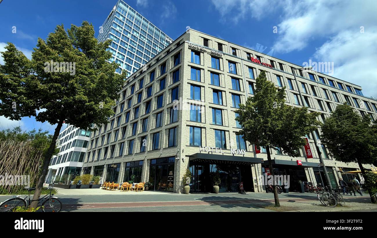 Modernes Hotelgebäude Romy mit großen Glasfenstern und Außensitzbereich, Fahrräder am Straßenrand in einer städtischen Umgebung geparkt Stockfoto