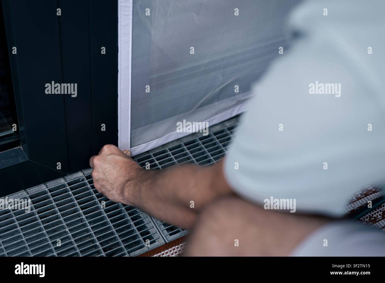 Weißes Moskitonetz, das im Fensterrahmen befestigt wird, veranschaulicht die präzise Befestigung in der praktischen Hauswartung. Stockfoto