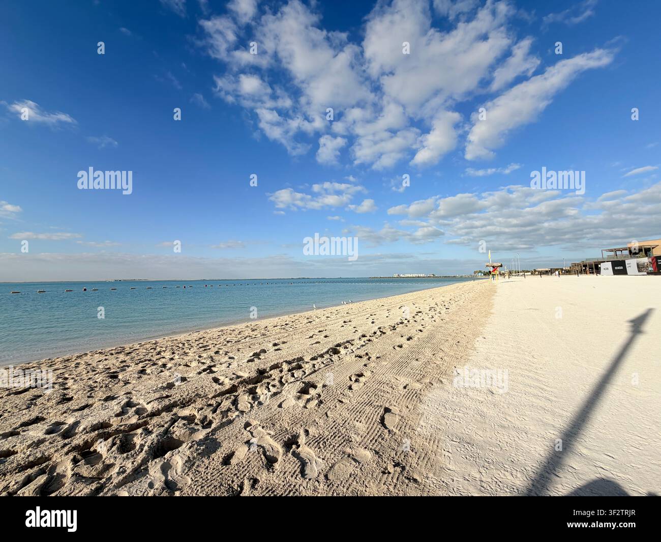 Panoramablick auf Hudayriyat Beach mit ruhigem blauem Wasser, einem klaren Himmel und vereinzelten Wolken in Abu Dhabi, Vereinigte Arabische Emirate - Smartphone-aufgenommenes Stockfoto