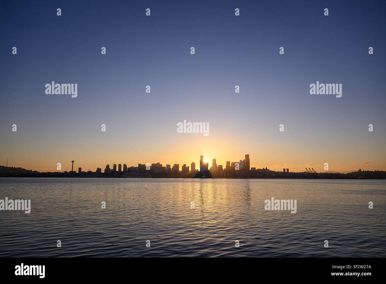 Blick auf die Skyline von Seattle bei Sonnenuntergang mit der Sonne hinter Wolkenkratzern, die sich auf den ruhigen Gewässern der Elliott Bay spiegelt, gesehen von der Don Armeni Boat Ramp aus Stockfoto