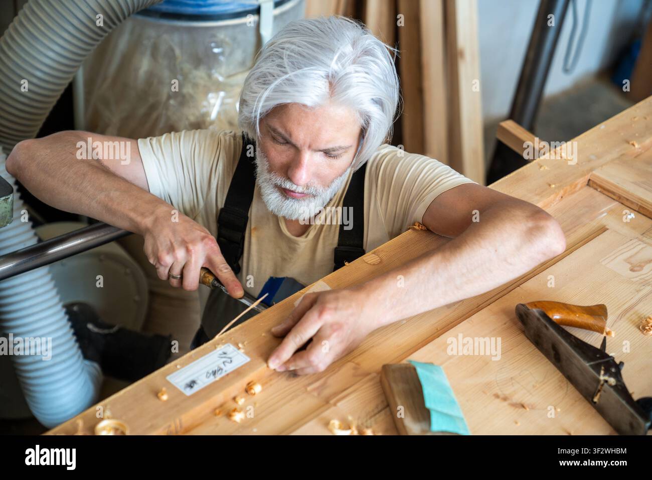 Konzentrierter Handwerker-Zimmermann arbeitet professionell mit einem Meißelwerkzeug und schnitzt Holzschichten an einer Tür Stockfoto