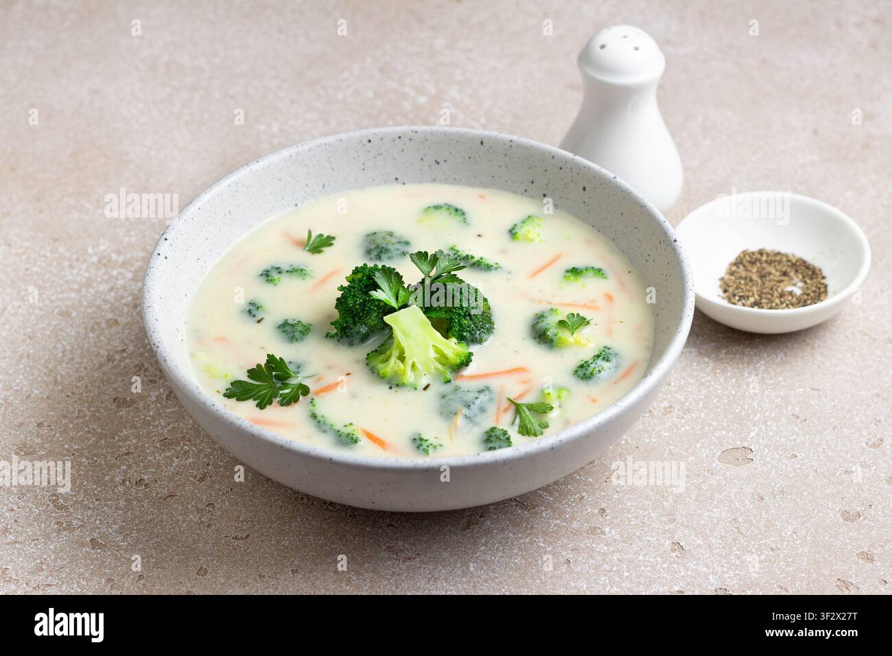 Hausgemachte cremige Brokkolisuppe mit Kartoffeln, Karotten und Petersilie in einer Keramikschüssel auf hellem, texturiertem Hintergrund Stockfoto
