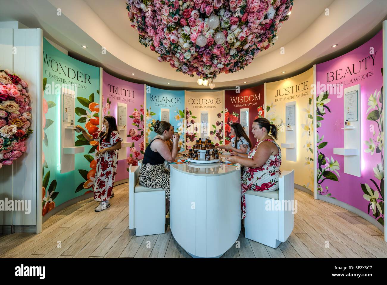 Ein Besucher testet einen Duft am Stand ‚Wunder‘ im Perfume Atelier der 7 Virtues in der Lower Water Street in Halifax, Nova Scotia, Kanada, während zwei andere Frauen Flaschen am runden Probiertresen vergleichen. Die Wandpaneele, die von ‚Wahrheit‘ bis ‚Schönheit‘ beschriftet sind, führen die einzelnen Düfte der Marke auf, die 2010 gegründet wurde, darunter ‚Vanilla Woods‘ und ‚Strawberry Jam‘. Halifax, Nova Scotia, Kanada Stockfoto