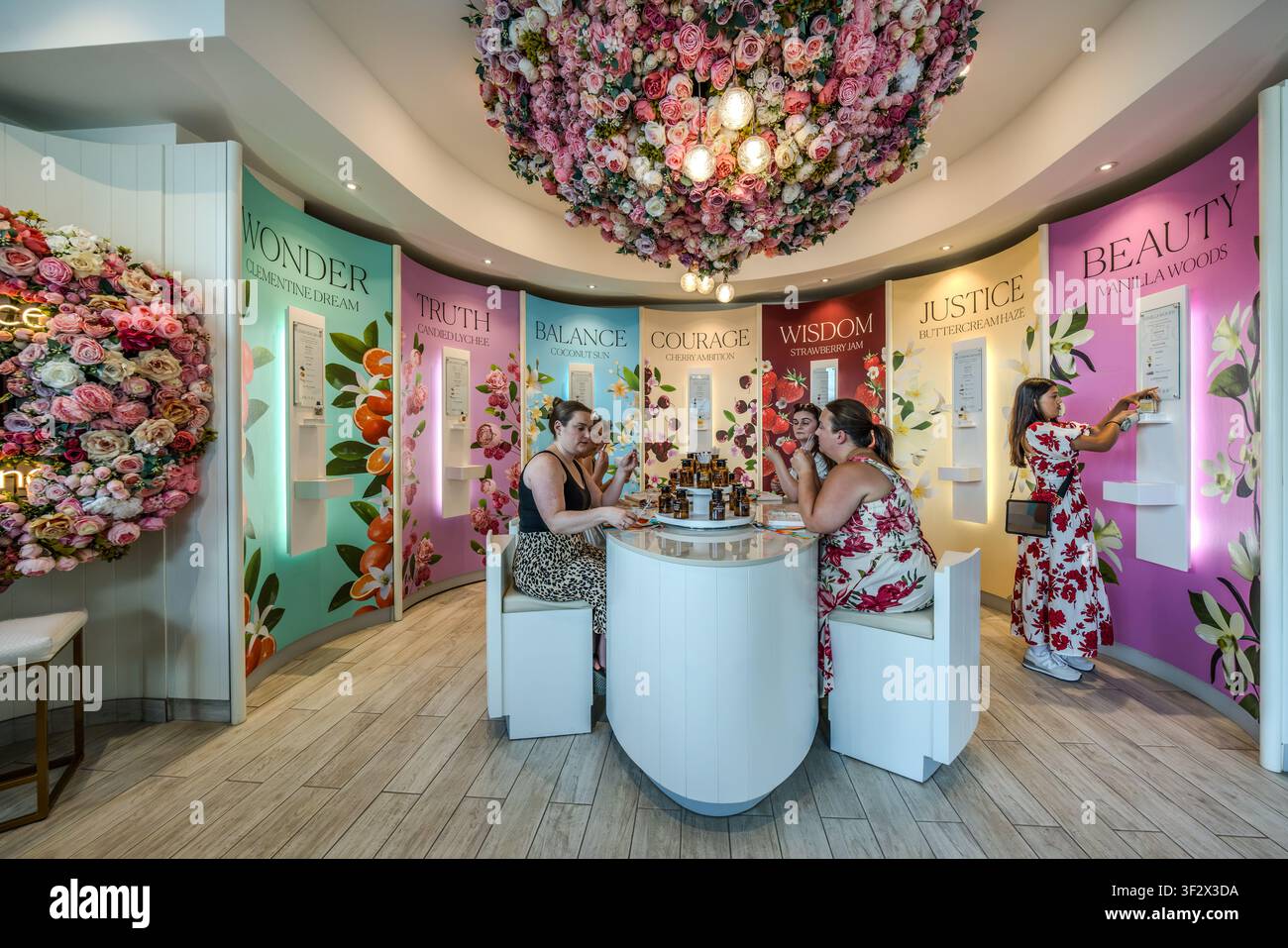 Besucher probieren Düfte am runden Probenstand im Perfume Atelier von The 7 Virtues in der Lower Water Street in Halifax, Nova Scotia, Kanada. Sieben Kabinen namens „Wunder“, „Wahrheit“, „Balance“, „Mut“, „Weisheit“, „Gerechtigkeit“ und „Schönheit“ repräsentieren die sieben Düfte der Marke, gekrönt von einer Kugel aus roten und rosa künstlichen Rosen. Halifax, Nova Scotia, Kanada Stockfoto