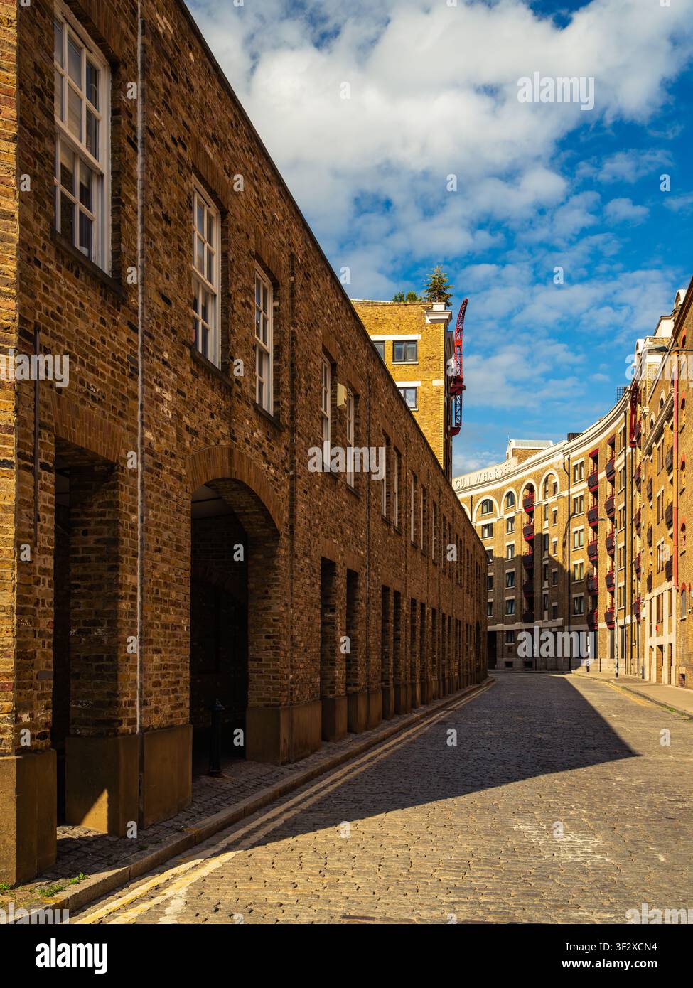 Sonnenbeschienene Kopfsteinpflasterstraße in London, gesäumt von historischer Ziegelwarenlagerhausarchitektur, die eine starke lineare Perspektive und Schatten zeigt. Stockfoto