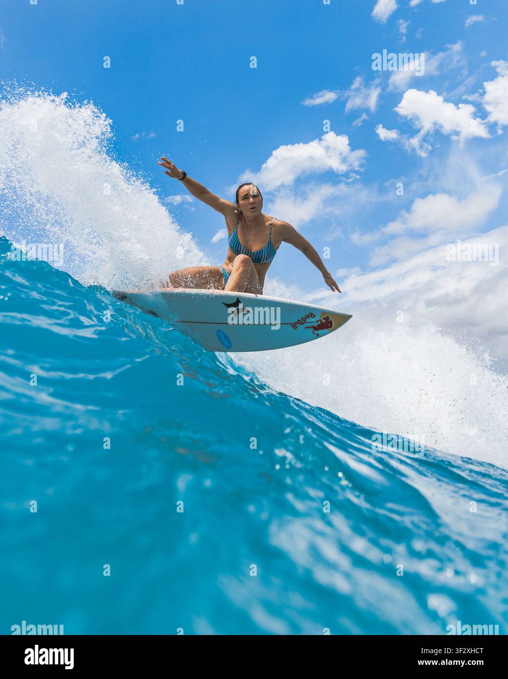 WAIKIKI, HONOLULU, HAWAII - 3. MAI 2022: Eine Frau in einem blauen Bikini dreht eine Bottomturn auf einem Shortboard, während Spritzer aufsteigen. Stockfoto