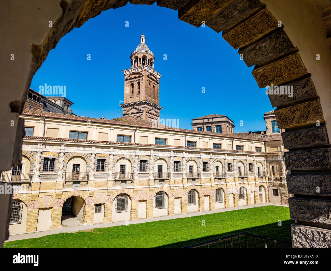 Palazzo Ducale zeigt seine historische Renaissance-Architektur und großen Glockenturm, gesehen durch einen alten Steinbogen, der den zentralen Innenhof einrahmt Stockfoto