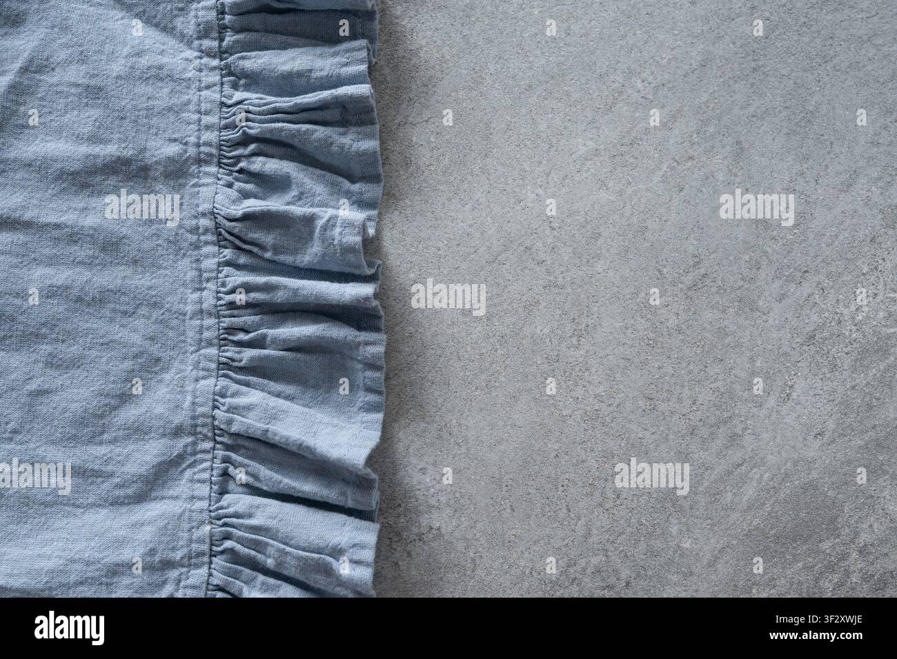 Blaues Leinen-Serviette auf grauem Stein-Hintergrund mit Kopierraum. Minimaler Textilhintergrund für Tischgedeck und Wohnkultur. Stockfoto