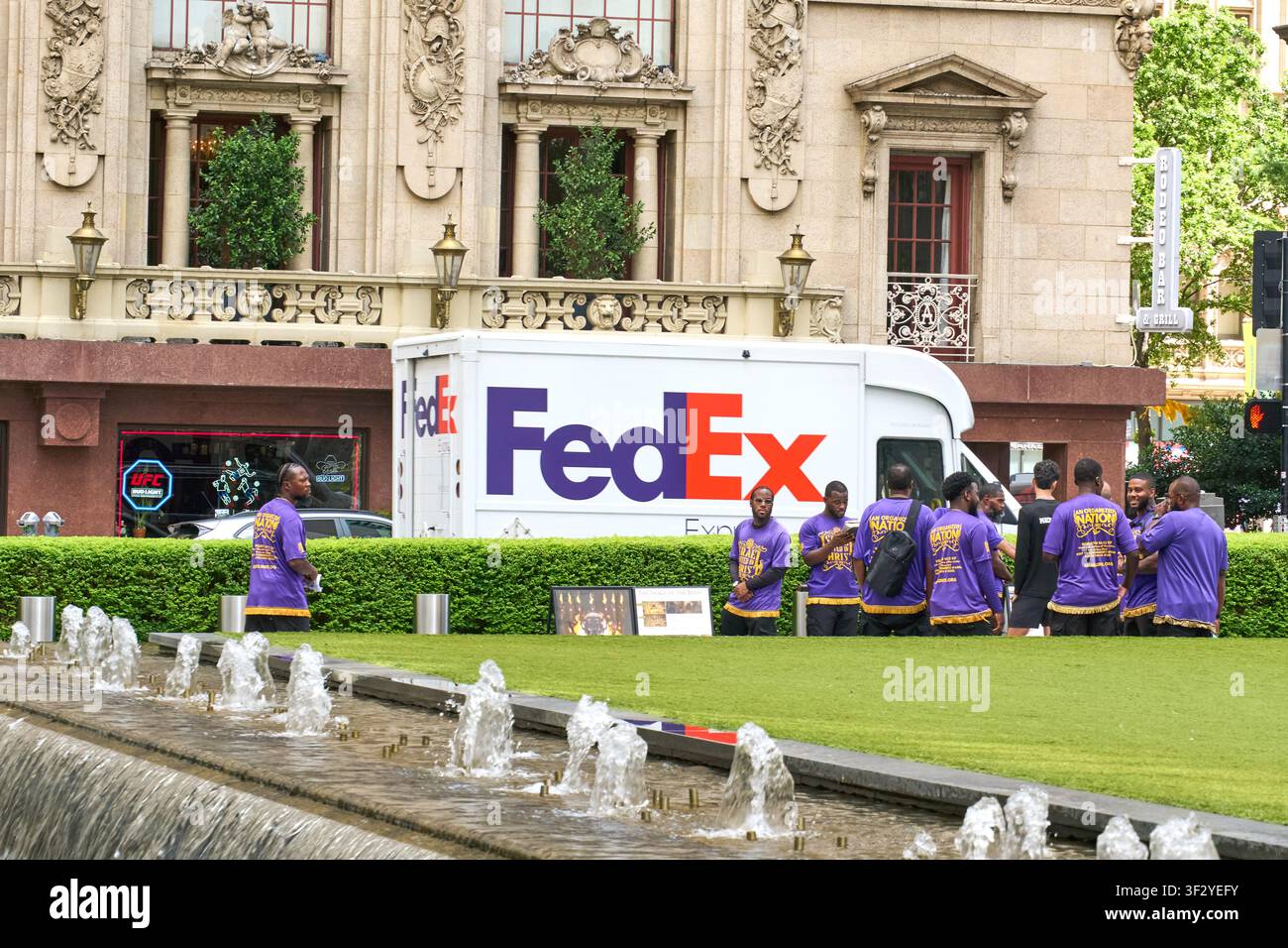 DALLAS, TX, USA - 11. JULI 2026: Ein FedEx-Lieferwagen ist vor einem prächtigen historischen Gebäude in Dallas, Texas, geparkt. Die Szene umfasst eine Gruppe Stockfoto