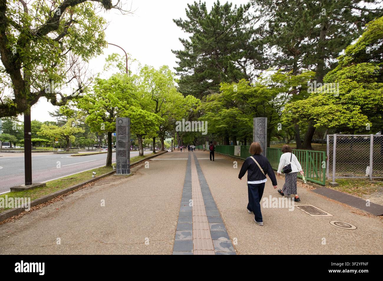 Fußgänger gehen einen von Bäumen gesäumten Weg in Noboriōjichō, Nara, Japan entlang. Das Bild fängt eine alltägliche Szene des städtischen Lebens in der Kansai-Region ein Stockfoto