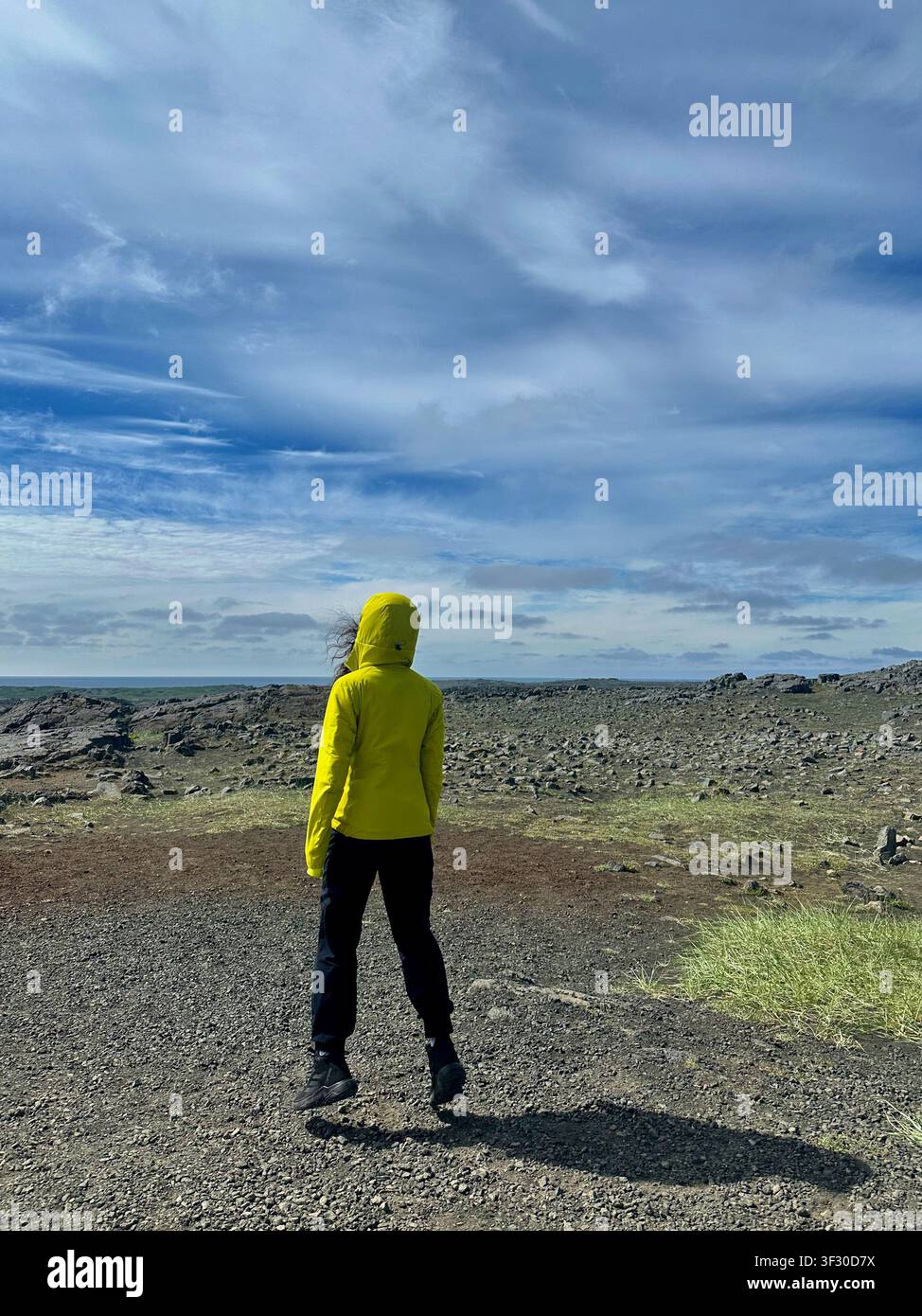 Frau springt auf dem Mars wie auf isländischem felsigem Boden unter einem bewölkten Himmel - Smartphone-aufgenommenes Stockfoto