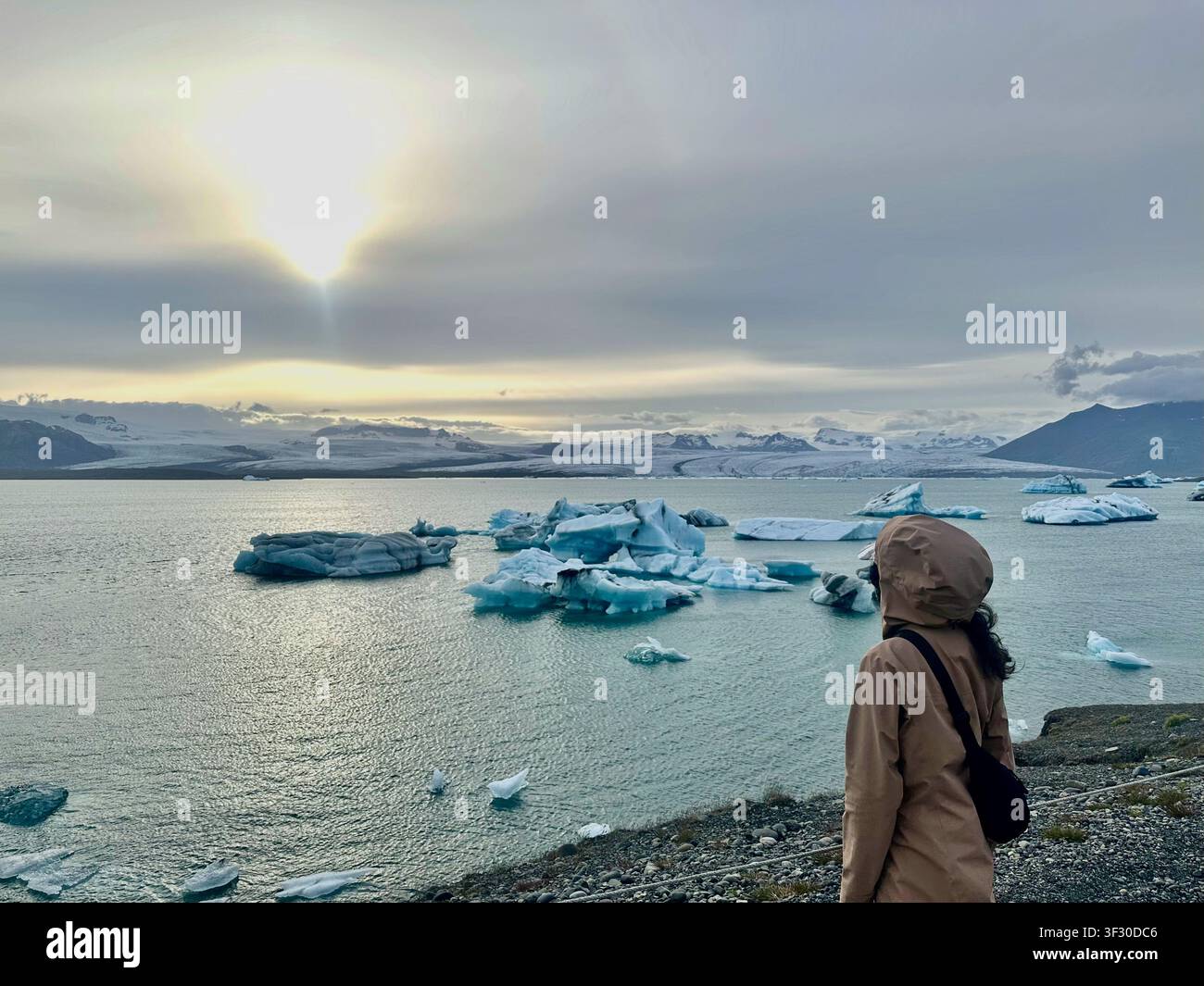 Frau bewundert den Blick auf die Gletscherlagune Jökulsárlón mit treibenden Eisbergen in der Dämmerung, Island - Smartphone-aufgenommenes Stockfoto
