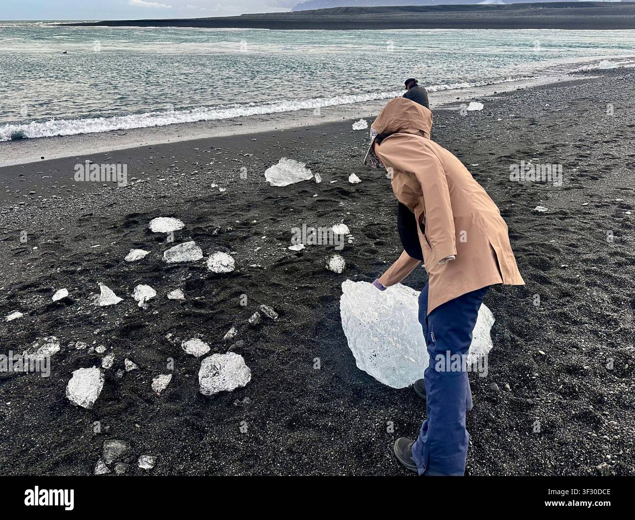 Frau berührt das an die Küste gespülte Eisberg am Diamond Beach mit schwarzem Sand, Island - Smartphone-aufgenommenes Stockfoto