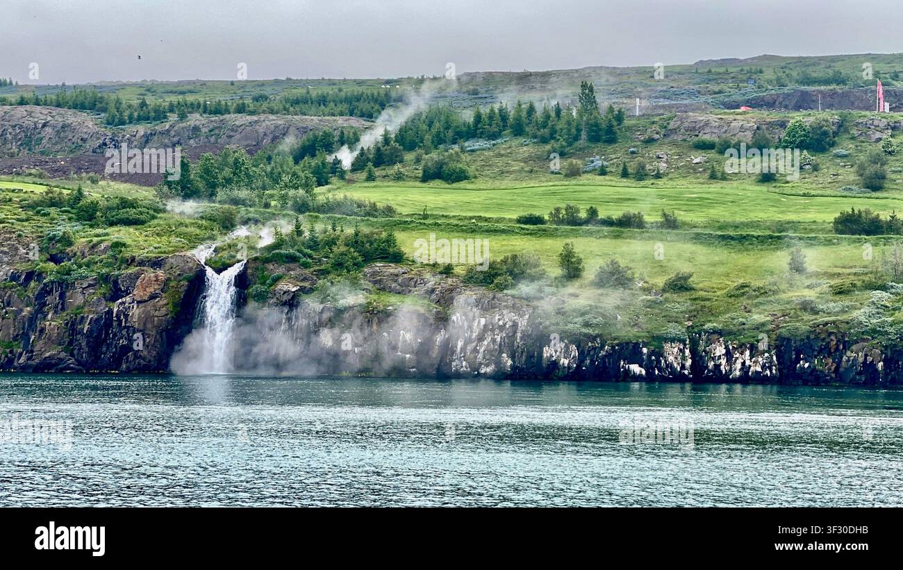 Die Ansicht eines heißen Quellen-Wasserfalls, der über die Klippe stürzt, von einem Walbeobachtungsboot aus, aufgenommen von Akureyri, Nordisland - Smartphone-aufgenommenes Stockfoto