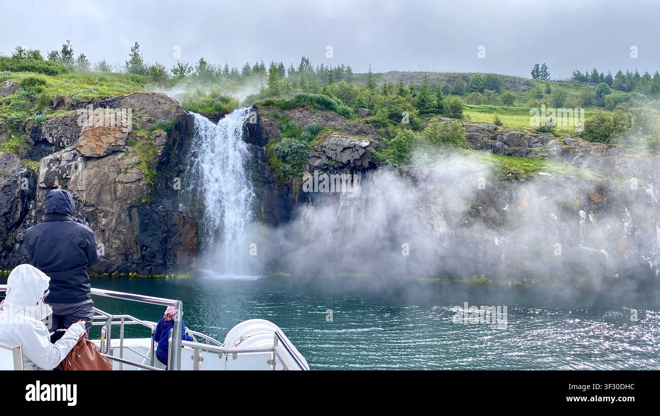 Die Ansicht eines heißen Quellen-Wasserfalls, der über die Klippe stürzt, von einem Walbeobachtungsboot aus, aufgenommen von Akureyri, Nordisland - Smartphone-aufgenommenes Stockfoto