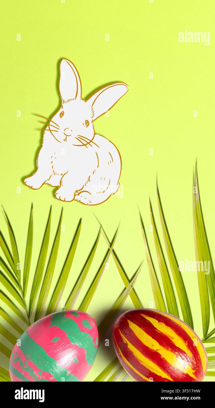 Ein kreatives Osterlayout auf einem limettengrünen Hintergrund mit einem handgezeichneten weißen Hasen, zwei farbenfroh bemalten Eiern und dekorativen Palmwedeln Stockfoto
