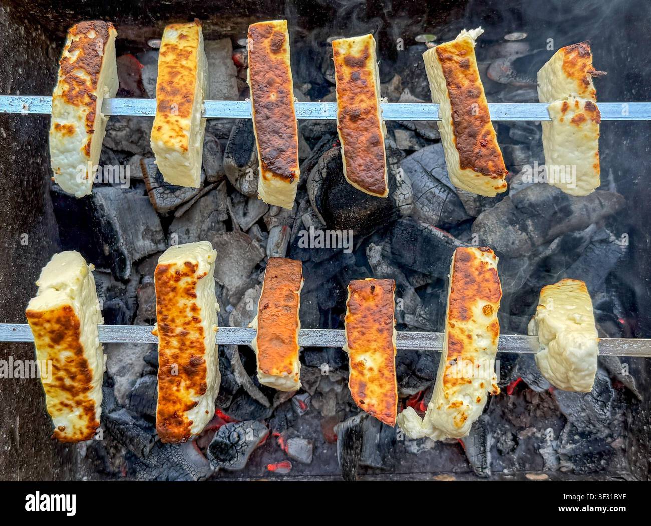 Käusescheiben, die auf Metallspießen über heißer Kohle in einer Grillgrube grillen Stockfoto