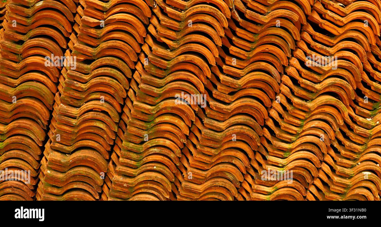 Nahaufnahme von gestapelten orangefarbenen Ziegelwellplatten mit welligen Mustern und grünem Moos, die einen texturierten architektonischen Hintergrund für Gebäudedesigns schaffen. Stockfoto