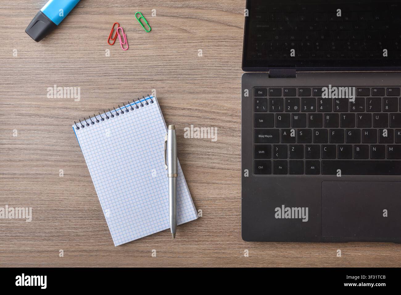 Top-Ansicht eines hölzernen Bürotisches mit einem Laptop, Spiralblock, Stift, Büroklammern und Marker. Sauberes Arbeitsplatzkonzept mit Kopierraum. Stockfoto