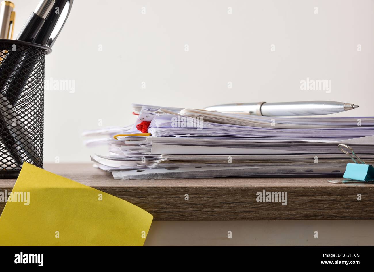 Seitenansicht eines Stapels Bürodokumente mit Clips und einem silbernen Stift, der obenauf liegt, neben einem Netz-Stifthalter auf einem Holzschreibtisch. Stockfoto