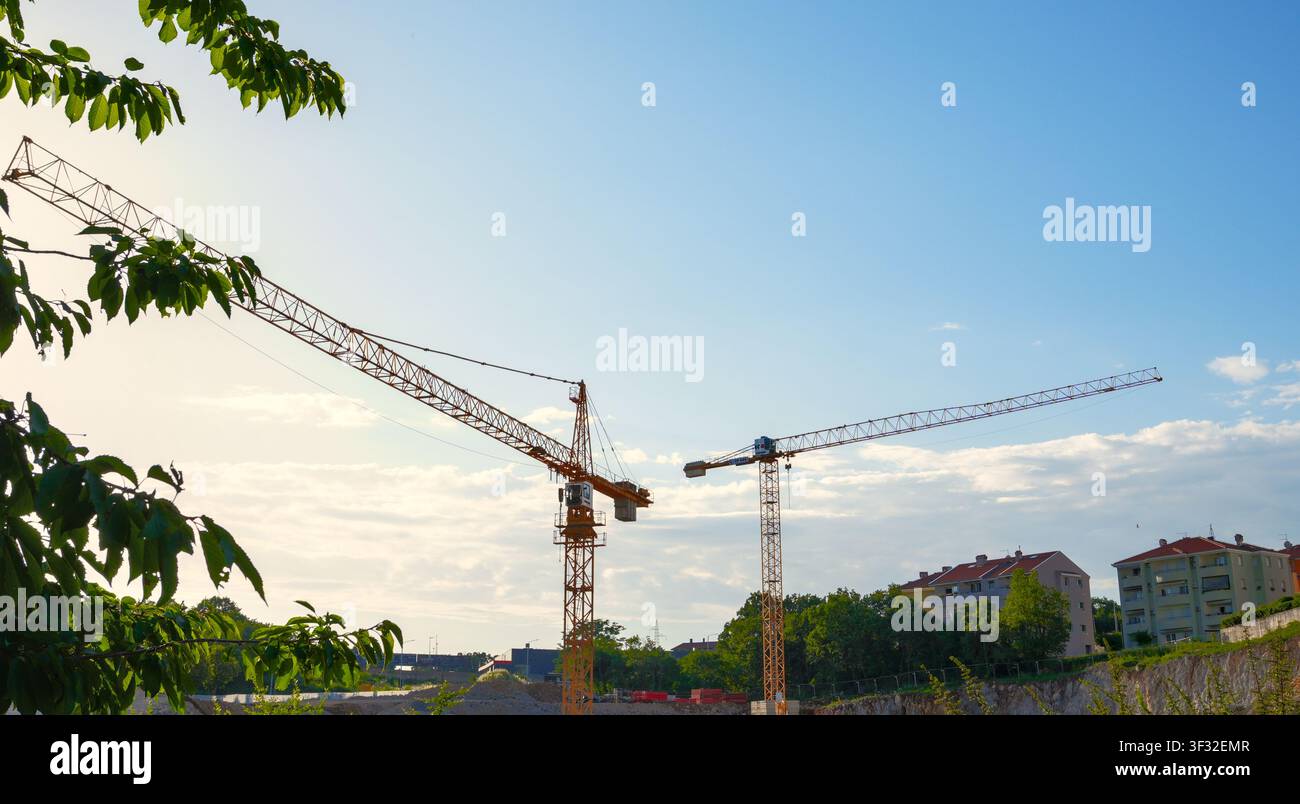 Vorübergehende Baukrane bauen eine neue Schule in Kastav, Kroatien, umgeben von Bäumen und Häusern. Stockfoto