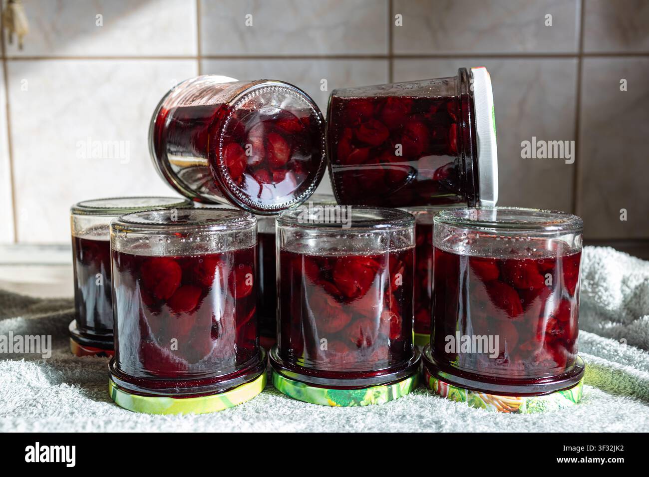 Sechs Gläser dunkelroter Kirschmarmelade in zwei Reihen angeordnet, hausgemachte süße Beerenkonfitüre und Einmachvorbereitung auf rustikalem Küchentisch, Frontansicht Stockfoto