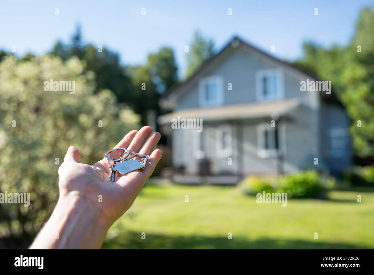 Hand, die Hausschlüssel vor einem unscharfen Haus hält Stockfoto