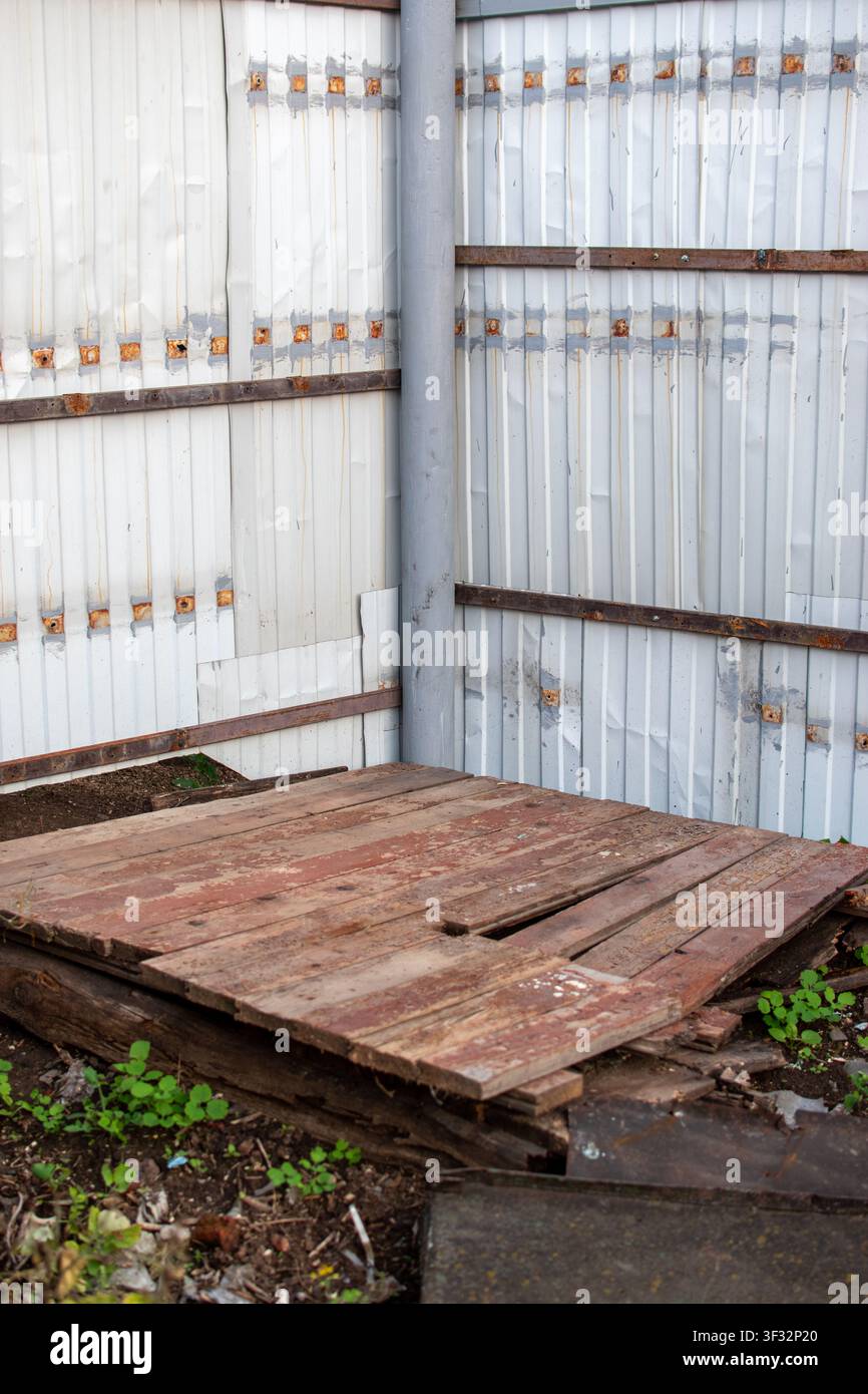 Alte zerbrochene Holzplattform auf dem Boden in der Nähe eines Metallzauns Stockfoto