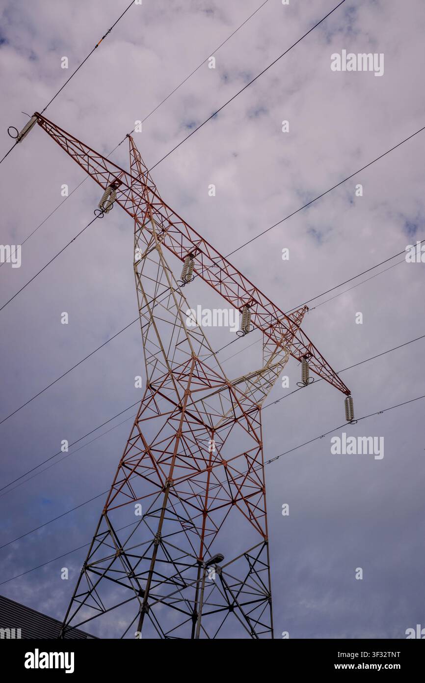 Hochspannungsmast-Struktur, die Stromleitungen gegen einen bewölkten Himmel stützt Stockfoto