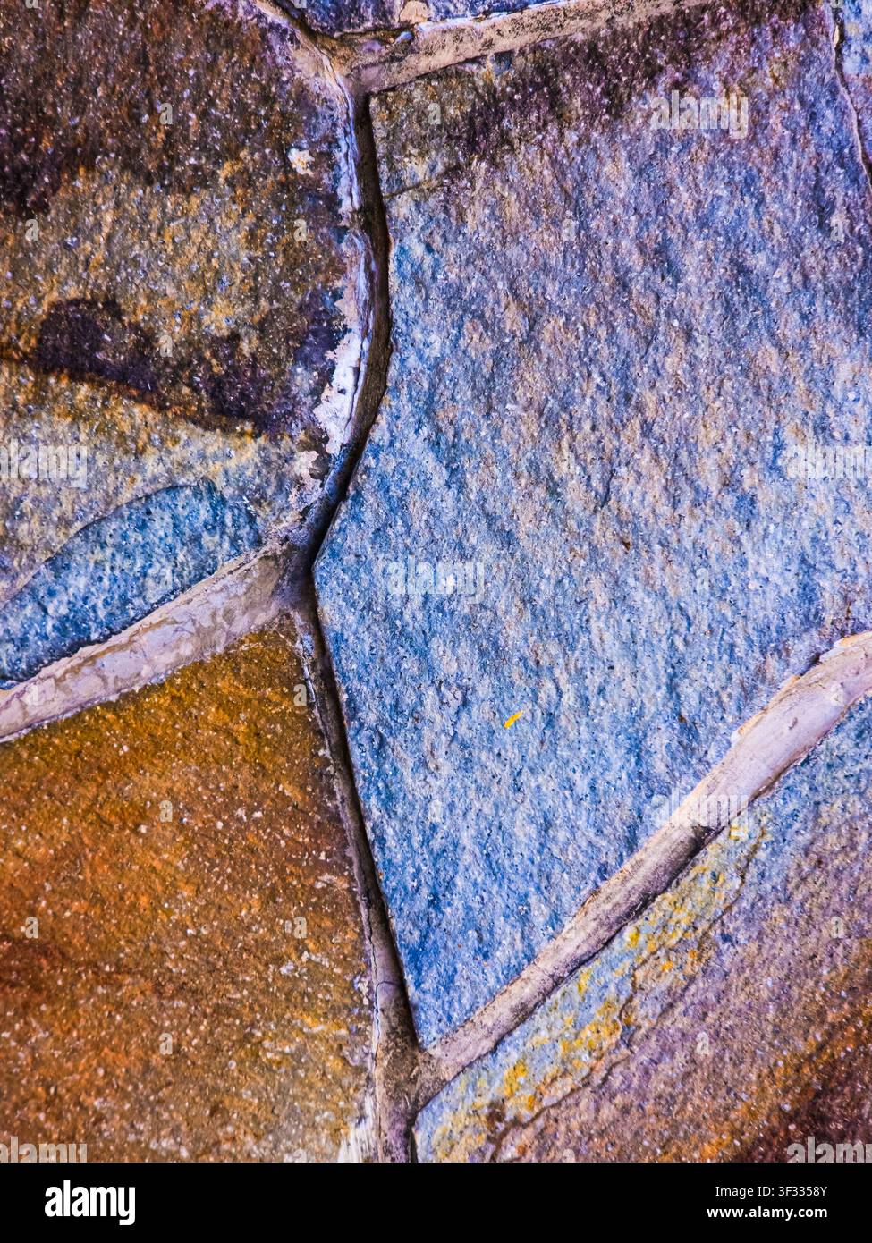 Nahaufnahme einer Natursteinwand mit Steinplatten in Blau- und Erdtönen, verbunden durch Mörtel. Ideal für Hintergründe. - Smartphone-aufgenommenes Stockfoto