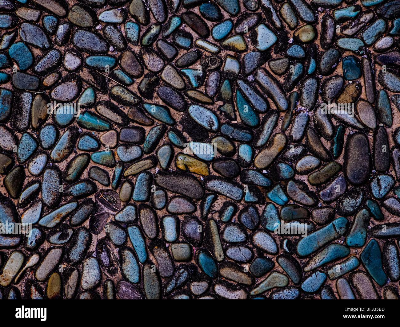 Top-Down-Ansicht von glatten, polierten Kieselsteinen, die in Beton eingebettet sind, mit einer Mischung aus blauen, grauen und erdigen Tönen. Ideal für Texturen und Hintergründe. - Smartphone-aufgenommenes Stockfoto