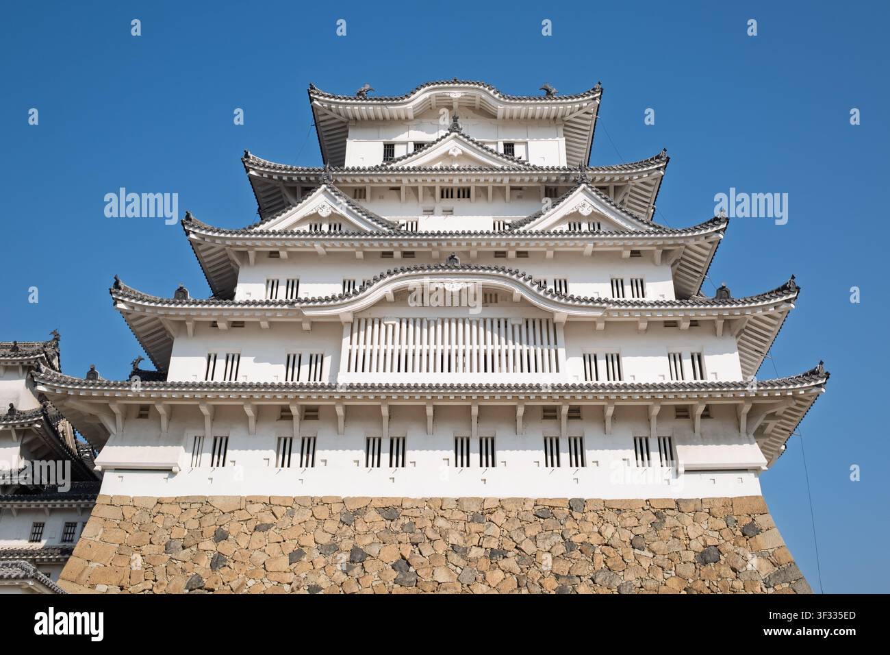 Direkte Frontansicht aus niedriger Perspektive der symmetrischen, gestuften weißen Fassade und der goldenen Turmspitzen des Hauptgebäudes des Himeji-Schlosses, Japan. Stockfoto
