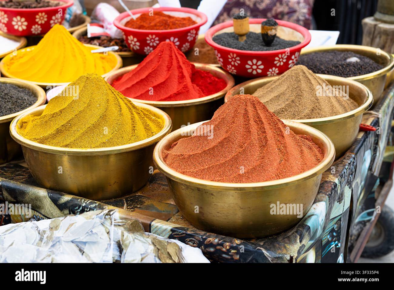 Grundgewürze, die in kegelförmigen Hügeln in Messingschalen auf einem traditionellen Basar in Buchara, Usbekistan, ausgestellt sind. Lebendiges gelbes Kurkuma, roter Paprika und Stockfoto