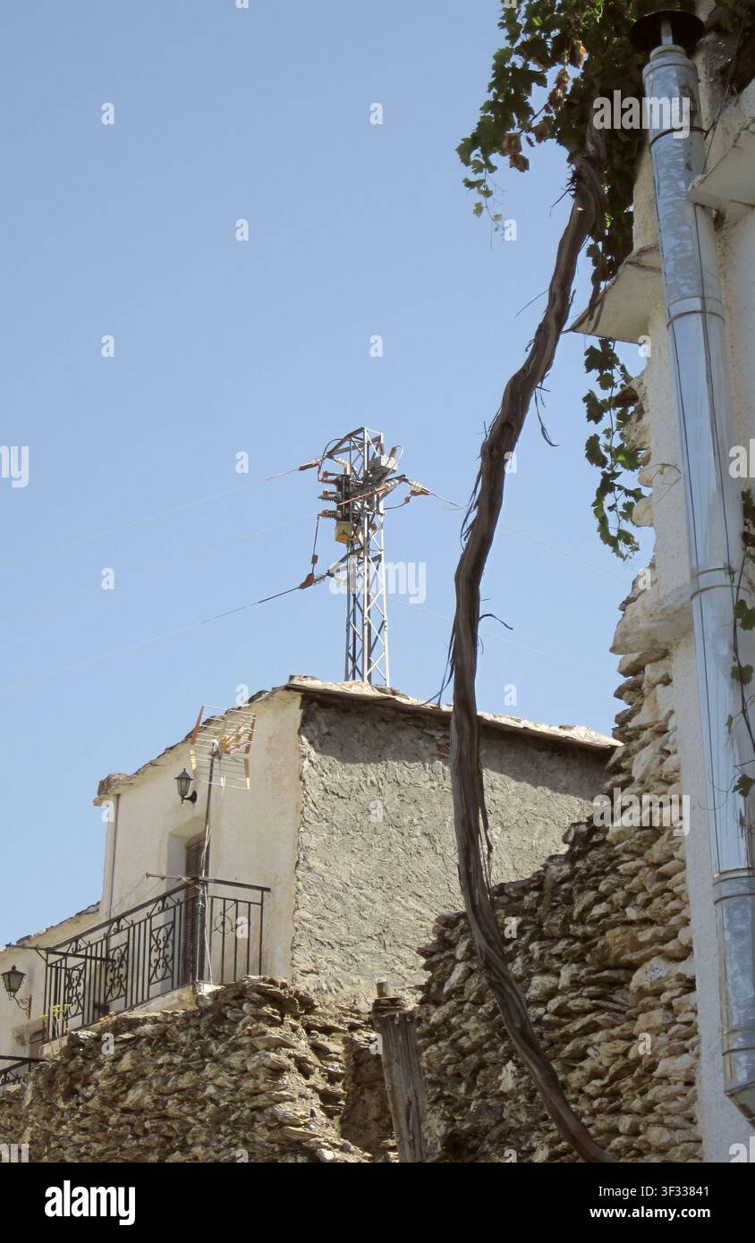 Kontrast in Bubion mit dem Stamm einer Weinranke, die die rustikale Mauer zur Terrasse hin hinaufklettert, und einer hochmodernen Antenne auf einem kleinen alten Haus Stockfoto