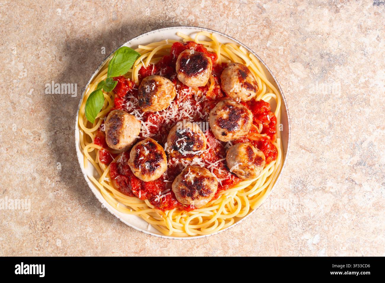 Ein Teller mit klassischen Spaghetti, garniert mit gebräunten Fleischbällchen und reichhaltiger Tomatensauce auf einem leichten Keramikgericht. Stockfoto